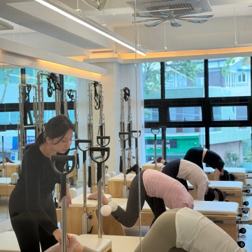 리포머에 엎드려 상체를 숙인 회원의 자세를 봐 주는 강사.