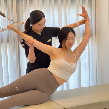 뒤에서 회원의 두 팔을 잡아 어깨를 열어 주는 강사.