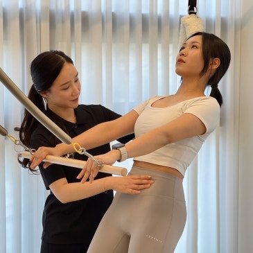 서 있는 회원의 팔을 스프링에 걸어 잡아 주는 강사.
