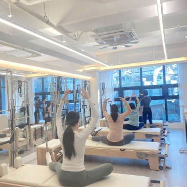 리포머에 앉아 두 팔을 위로 뻗은 회원들의 뒷모습.