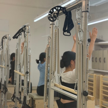 캐딜락 기구 앞에서 두 팔을 위로 뻗어 올린 회원들의 그룹 수업.