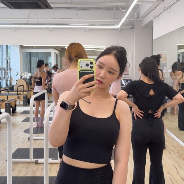 스튜디오 거울 앞에서 휴대폰을 들고 선 모습과 뒤편에서 수업 중인 사람들.