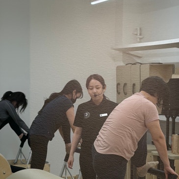 체어 앞에서 상체를 숙인 회원들과 가운데에서 지켜보는 강사.