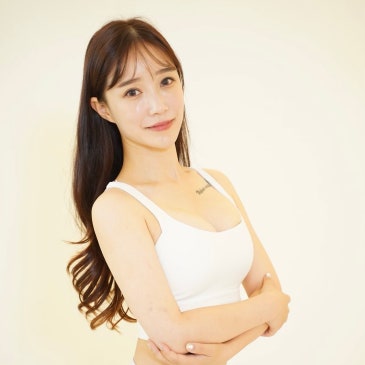 밝은 배경 앞에서 팔짱을 끼고 정면을 보는 흰 운동복 차림의 여성.