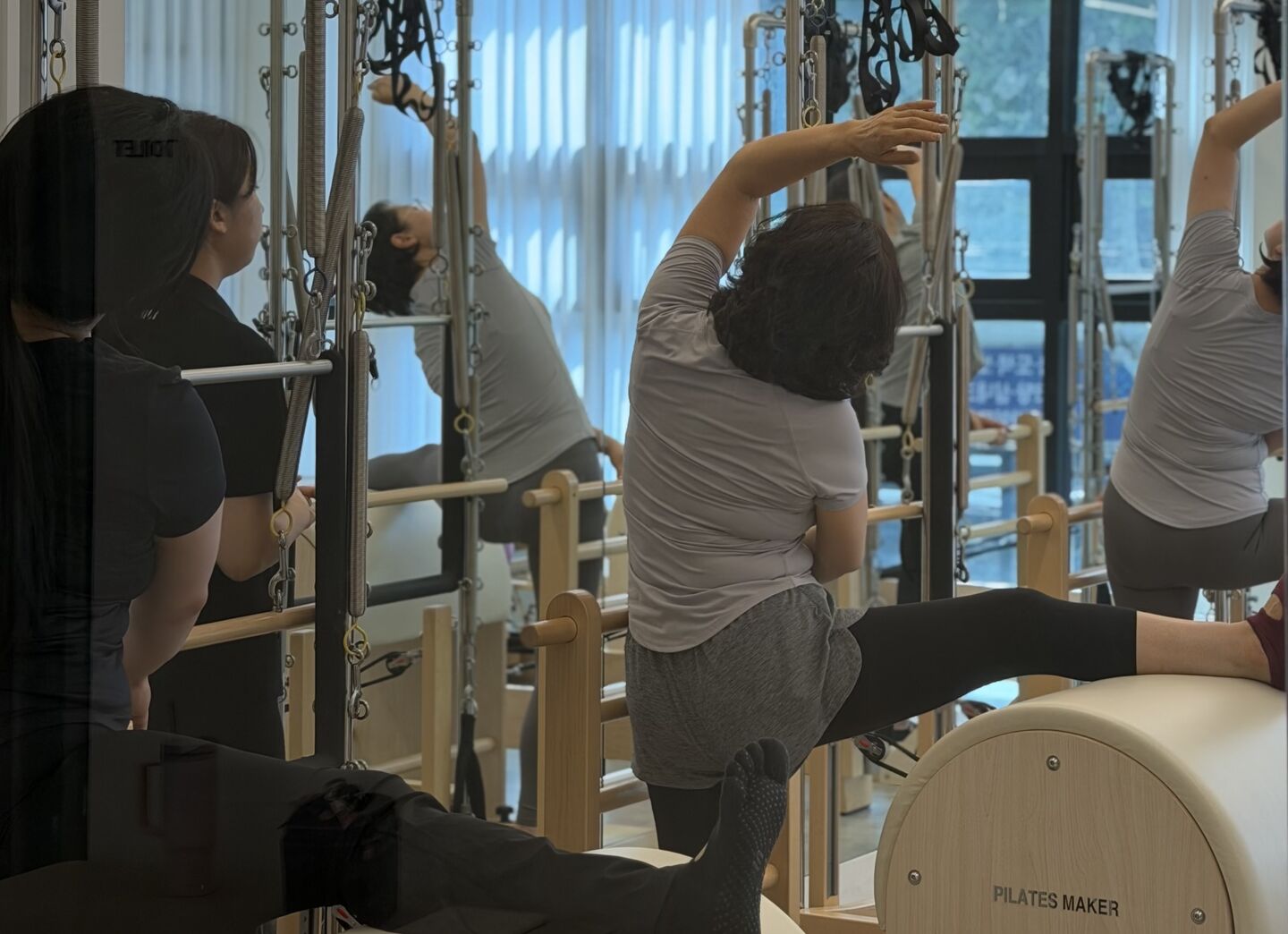 래더배럴에 상체를 얹고 스트레칭하는 회원 세 사람과 자세를 봐 주는 강사.